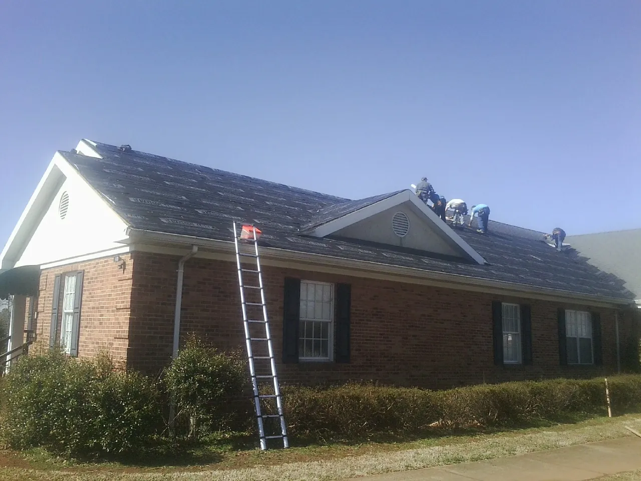 Crew tearing shingles off a brick ranch roof with a ladder set — Metal Roof Repair work by our crew in Pierrepont Manor