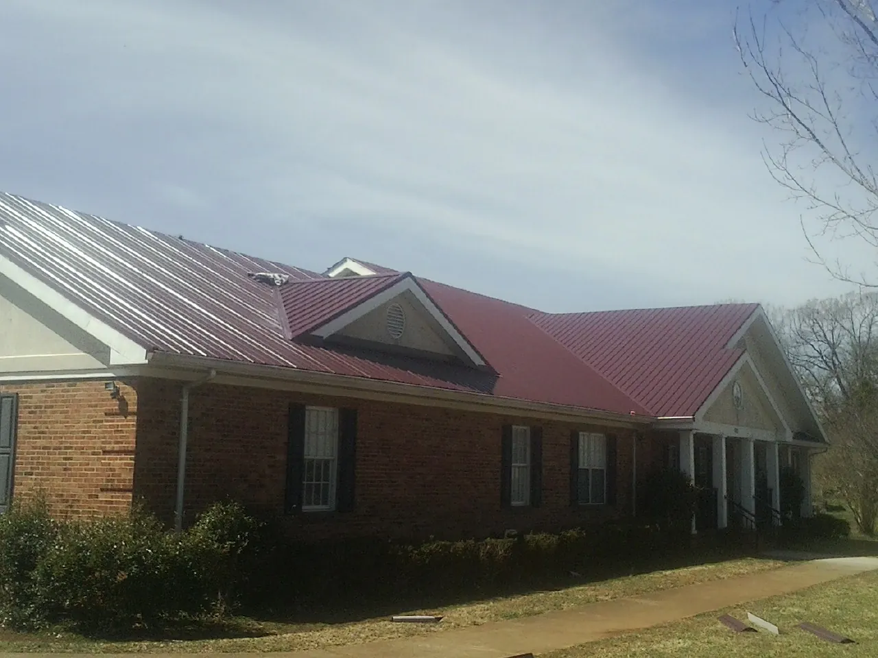Red metal roof with gabled entries on a long brick building, from a Hail Damage Roof Repair job in Pierrepont Manor
