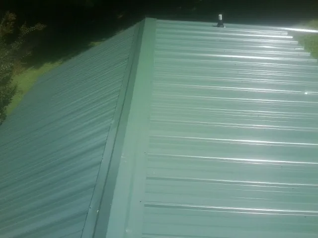 New green metal panels meeting at the ridge of a roof — Flat Roof Repair work by our crew in Pierrepont Manor