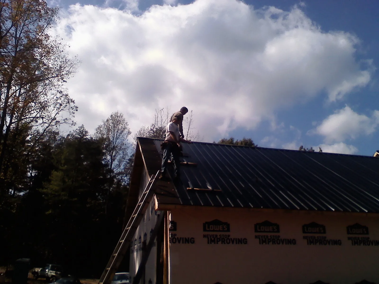 Roofer fastening dark metal panels high against a cloudy sky, from a Roof Inspection job in Pierrepont Manor