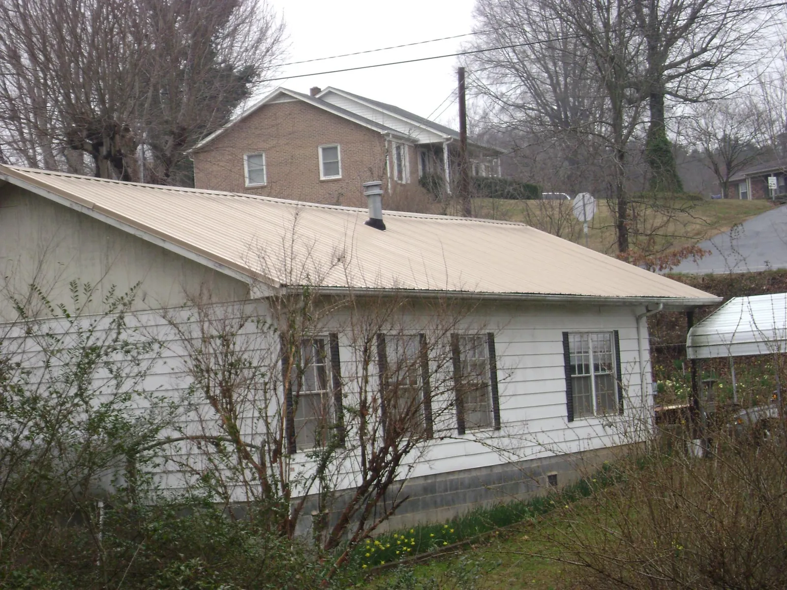 Tan metal roof on a white sided house set into a hillside — Commercial Roofing by Roofing Brothers in Pierrepont Manor