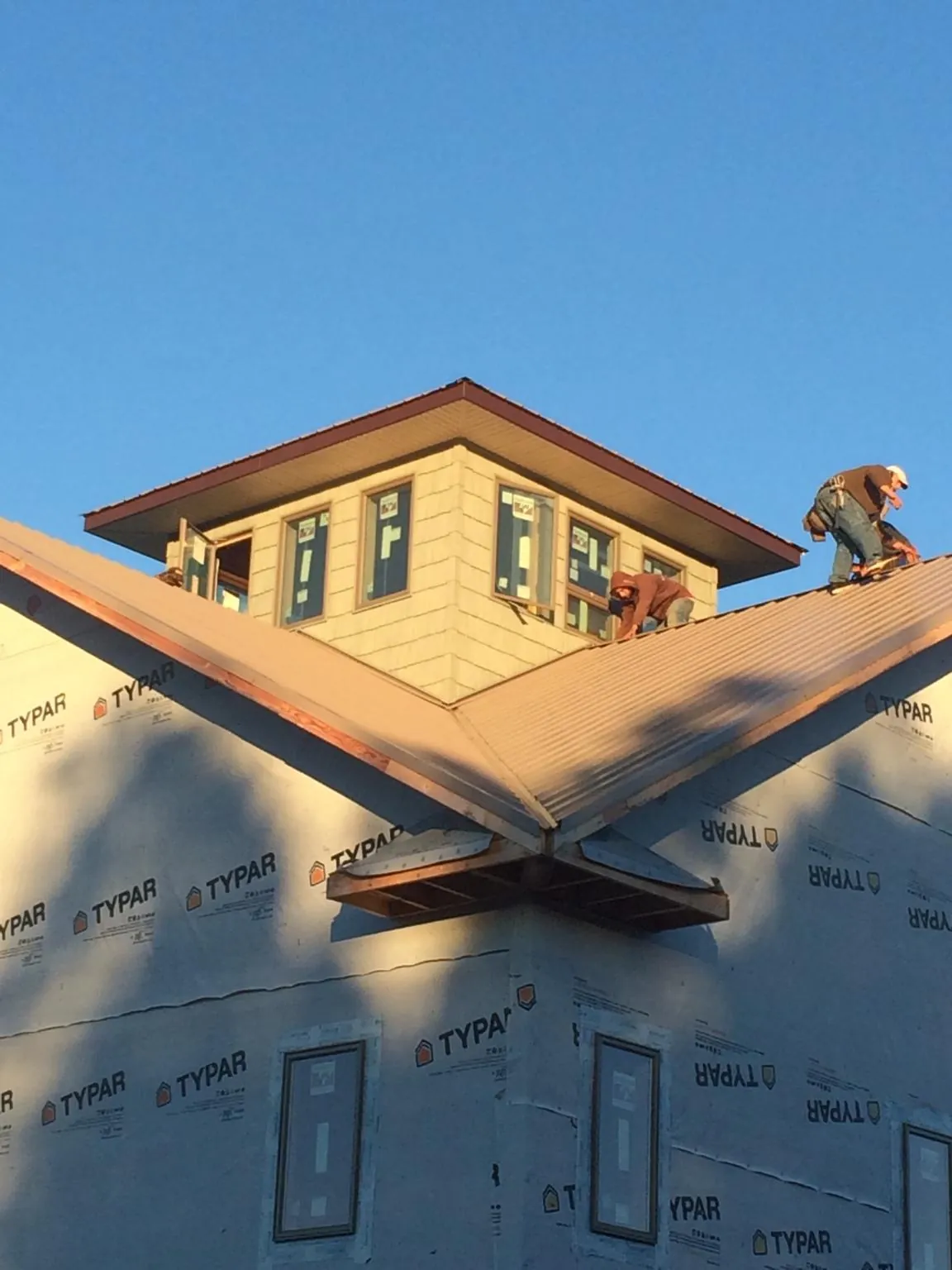 Roofers working around a rooftop cupola on a new metal roof at sunset — Roof Waterproofing in Pierrepont Manor by Roofing Brothers